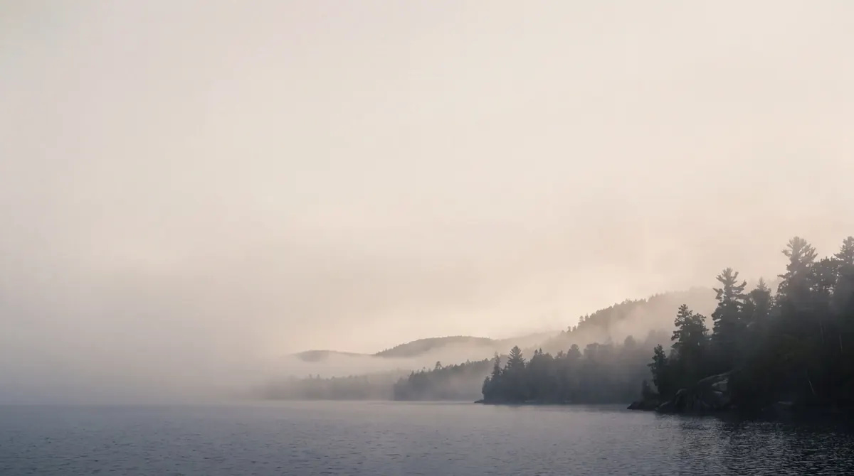 Dawn mist drifting over still water and layered pine ridges in the Minnesota woods